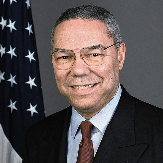 Official portrait of Colin Powell wearing a dark suit and glasses with an American flag hanging behind him