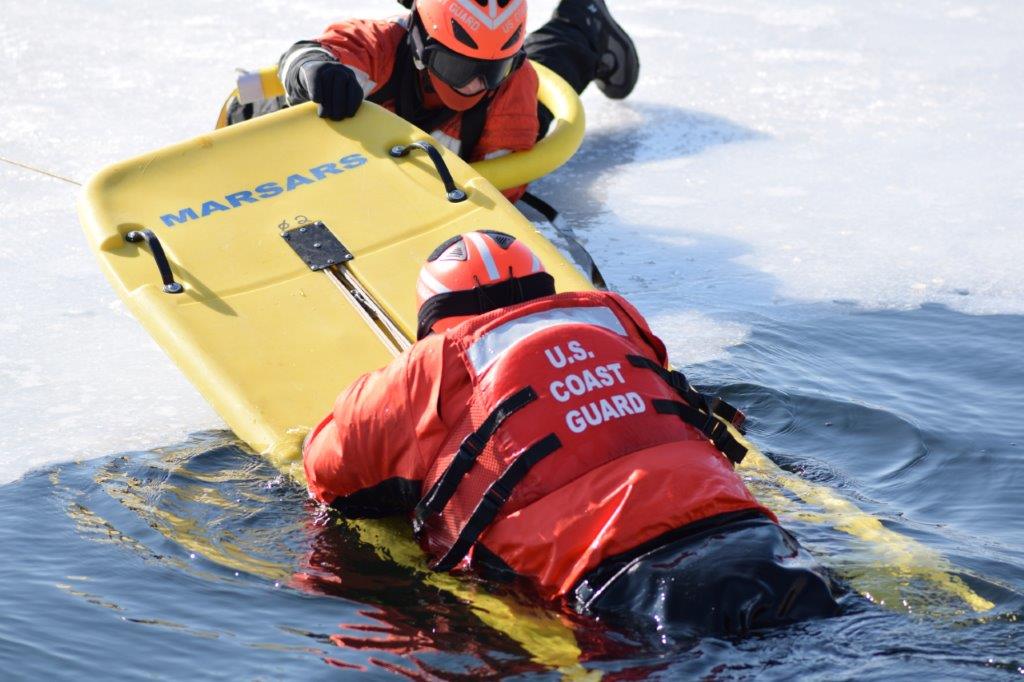 USCG member on ice performing a practice rescue of other member in water