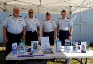 The four members, all in tropical blue uniform, stand behind the display table under the Flotilla 12-01 canopy