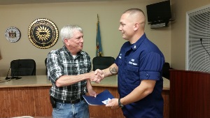 Jerry, at left, smiles while shaking hands with Chief Holcomb, as they both hold the award certificate