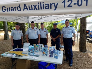 From left to right, Bob Lesperance, Steve Straneva, Bruce White, John Craig (in ODU) and Joe Harris face the camera behind the table displaying safe boating items and literature. The Flotilla number is on the front panel of the canopy.
