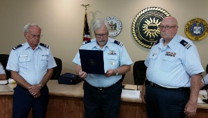 John Craig, at left, and Fran Doyle at right listen solemnly as Steve Straneva, between them, reads the Meritorious Team Commendation citation