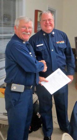 Bob Adams, in forefront at left, shakes hands with Mike Geletej as he holds his copy of written orders for 2013. Both are wearing Winter Dress Blue uniform.