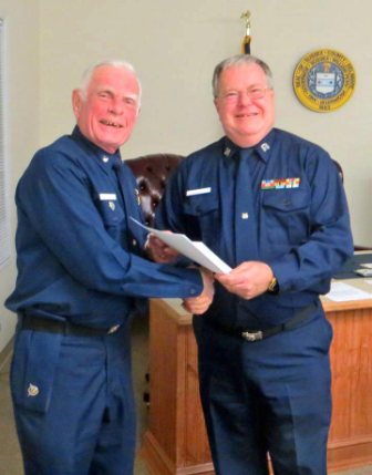 Bob Lesperance, facing camera at left, shakes hands with Mike Geletej as they hold the copy of the written orders for 2013. Both are wearing Winter Dress Blue uniform.