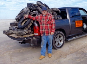 Dave, in casual wear, standings in front of a blue pick up truck piled high with used tires
