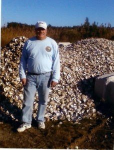 Dave, in casual wear, stands in front of a pile of oyster shells nearly as high as he is