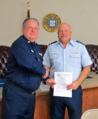 Mike Geletej, facing camera at left (wearing Winter Dress Blue), shakes hands with Dave Ritondo (wearing Trops) as Dave holds his copy of the written orders for 2013.