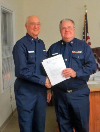 Joe Harris, facing camera at left, shakes hands with Mike Geletej as Mike holds his written orders for 2013. Both are wearing Winter Dress Blue uniform.