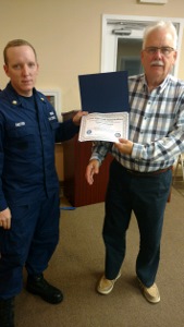 BM2 Raxter, in ODU at left, holds Denny's certificate with his left hand while Denny holds the bottom of the certificate with his left hand and prepares to shake hands