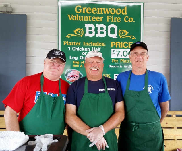 Mike Geletej (left), Dave Ritondo (center), and Joe Harris (right) smile as they wear green aprons and ball caps