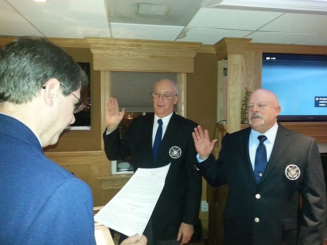 Mark Letavish, standing at left foreground (wearing Service Dress Blue), swears in Joe Harris and Dave Ritonda (in the blue blazer uniform, facing him with their right hands raised)