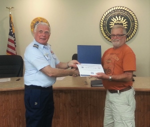 Bob Lesperance, at left in Tropical Blue, shakes hands with Richard Adams, in civilian clothes, while they both hold the certificate and face the camera
