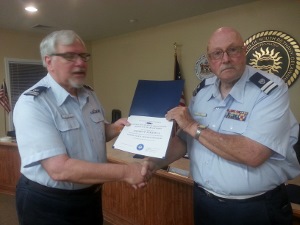Stephen, standing at left, shakes hands with Fran as they both hold the certificate