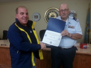 Todd, standing at left, shakes hands with Fran as Fran holds the certificate