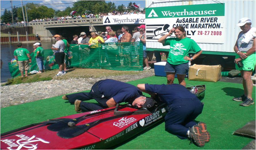 Two mens in Auxilairy Uniforms leaning over examining a canoe at the end of the race