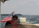 Man in a coast Guard Auxiliary Life Jacket and Unofrm driving a boat with an American Flag in the background also in the backgroun is a white and yellow which has been taken in tow