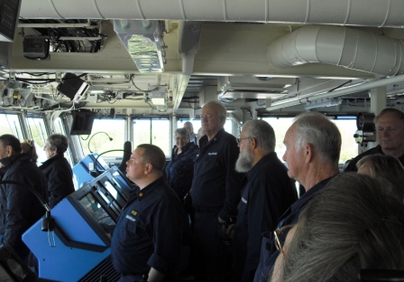 Several people in Auxiliary Uniforms standing on the Bridgeof highly computerize modern ship 