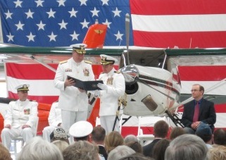 Several men in Summer white Coast Guard Uniforms in front of a large American nighttime d a white and blue small Aircraft 
