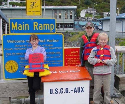 Photo of three children with life jackets standing next to Kids Don't Float life jacket box