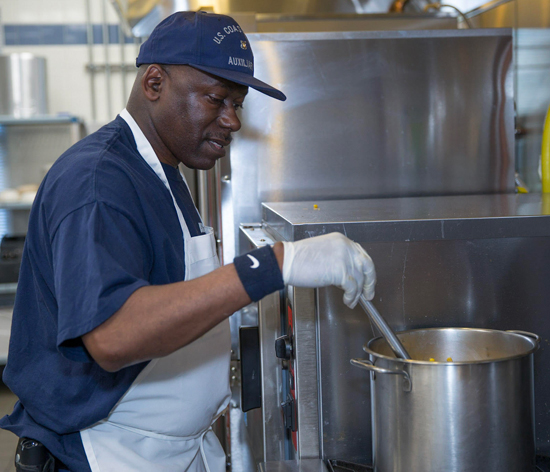 Aux Fred Knox in ODU and white apron stirring ingredients in a large pot in a kitchen