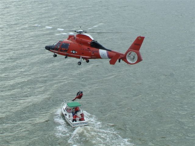 Coast Guard helicopter lowering man down to aux vessel 