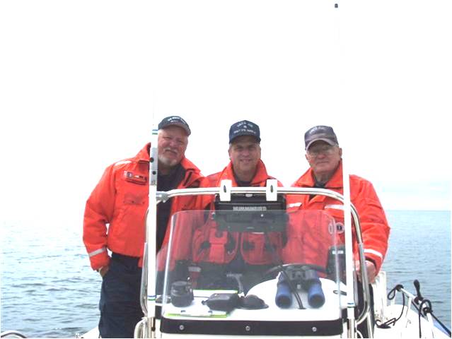 three men in Auxiliary uniforms and Orange Orange float coats on a boat 