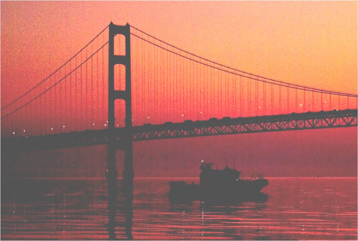 Picture of an Auxiliary Boat Crossing under the Mackinaw Bridge at Dawn with the sun rising in the background 