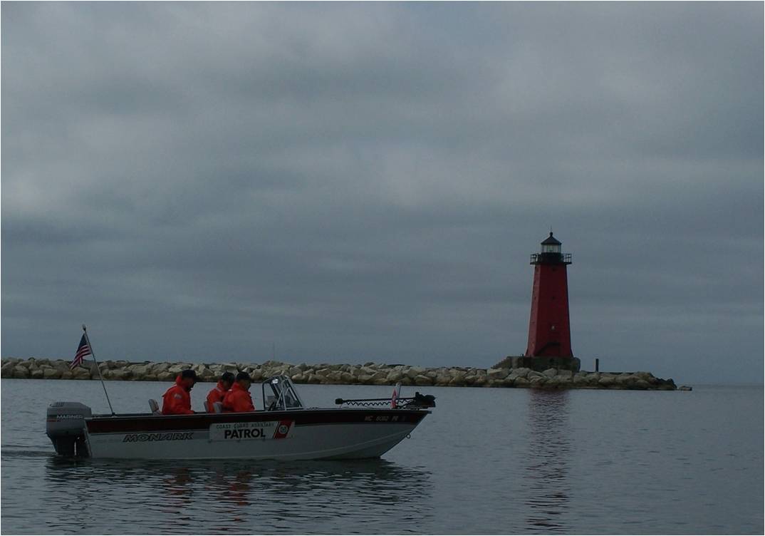 A small Auxiliary Patrol Boat going out to the water  past a red and black lighthouse 