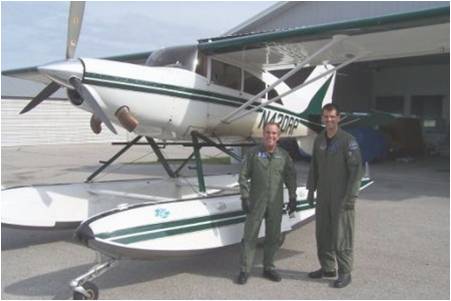 Two Men in Green Flight suits  standing next to a white plane with green stripes