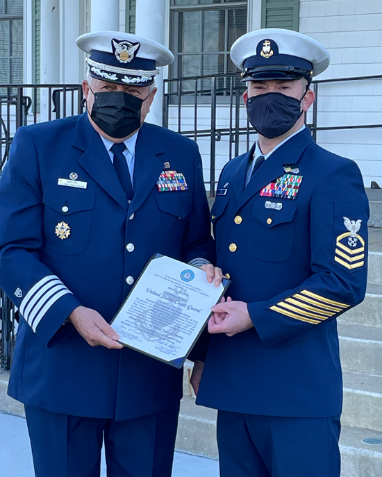 An auxiliarist in a mask poses with a chief petty officer, also in a mask, as they hold a certificate